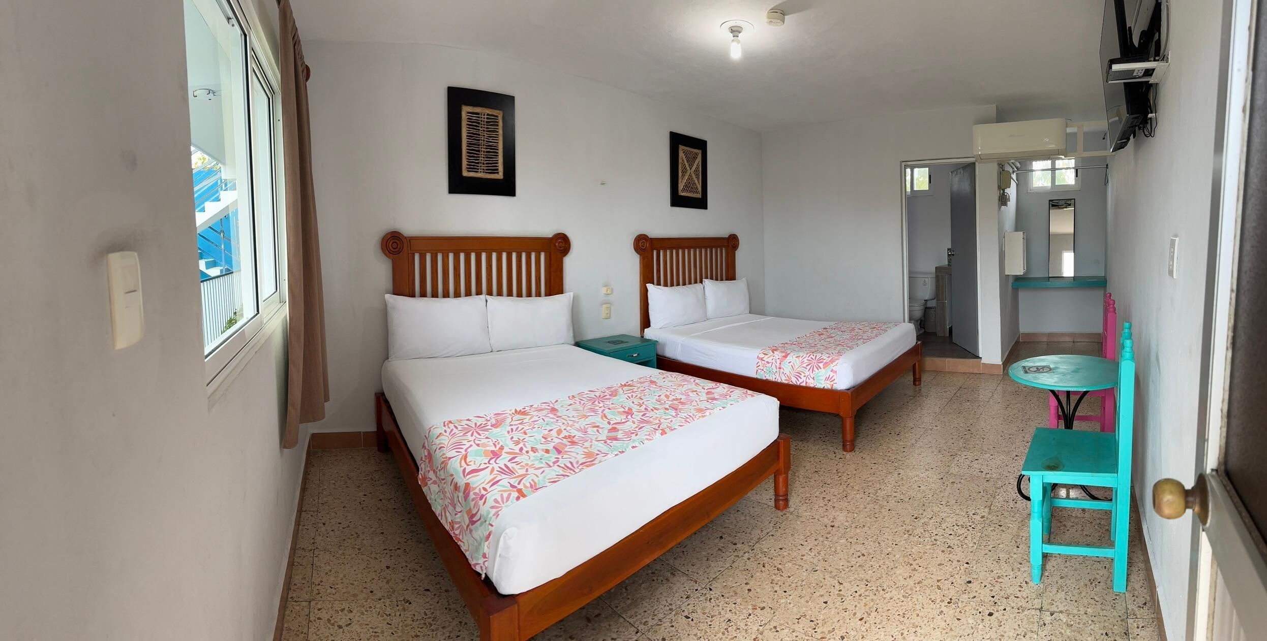 A hotel room with two wooden beds, a small table, and a chair.