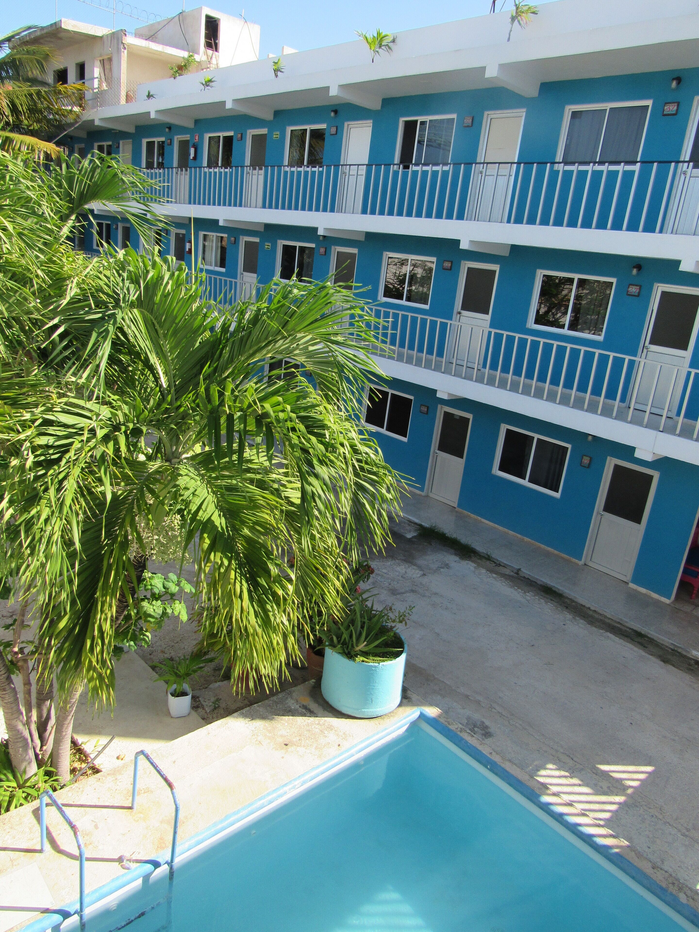 Un hotel de varios pisos con balcones, piscina y plantas en macetas.