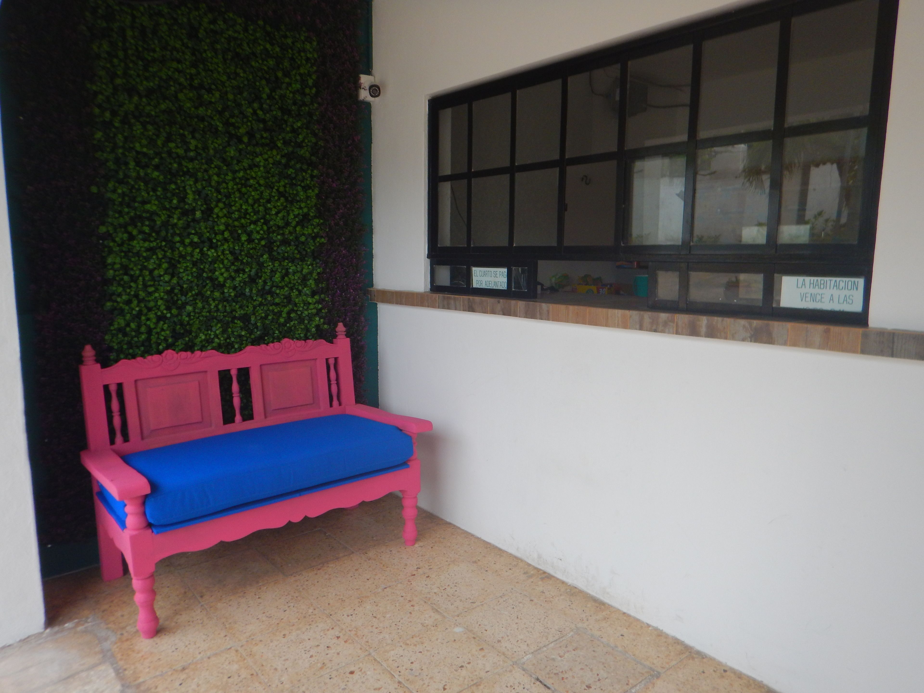 Eine pinkfarbene Bank mit blauer Sitzkissen in einem Raum, der eine grüne Wand und ein Fenster hat.