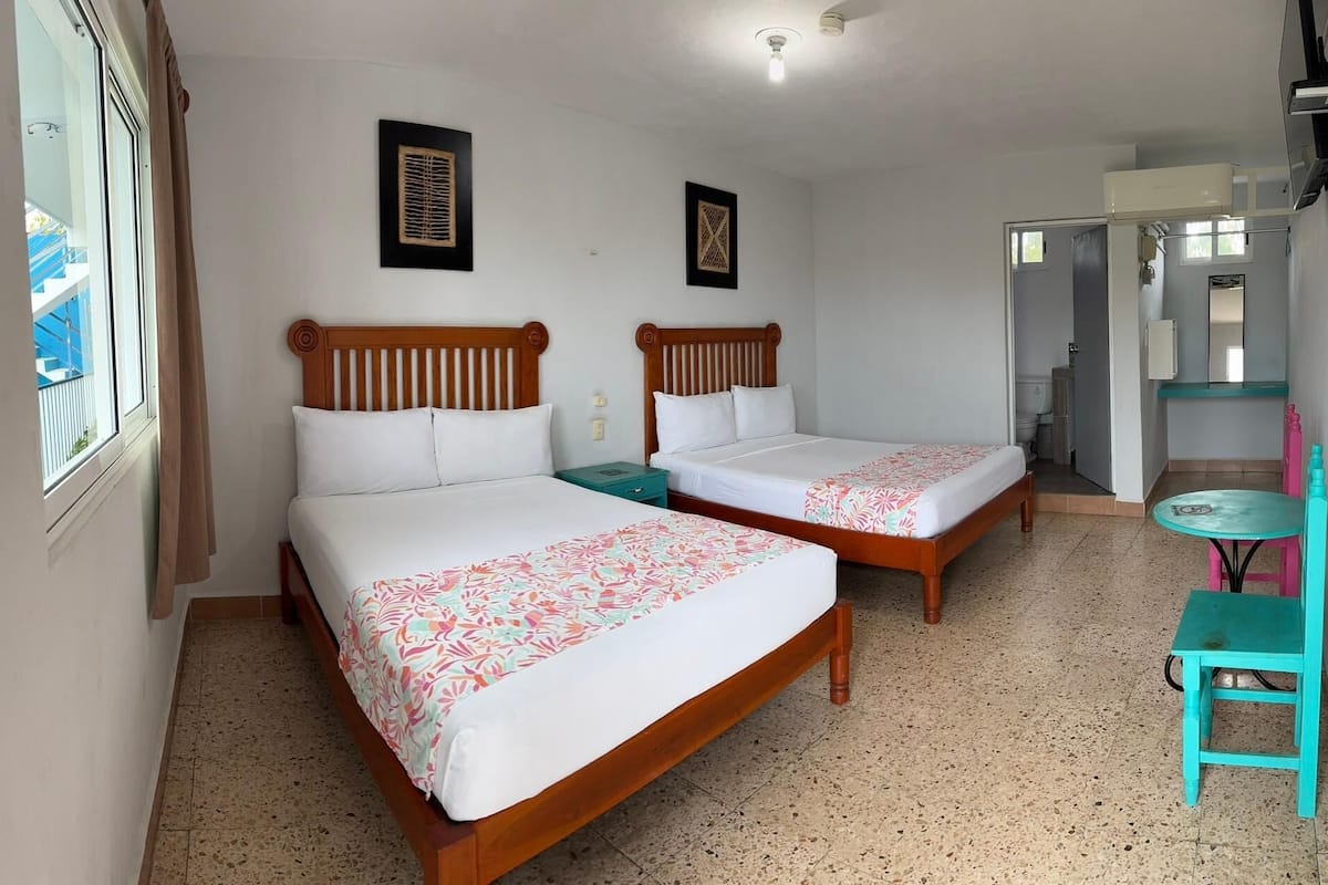 A hotel room with two wooden beds, a small table, and a chair.