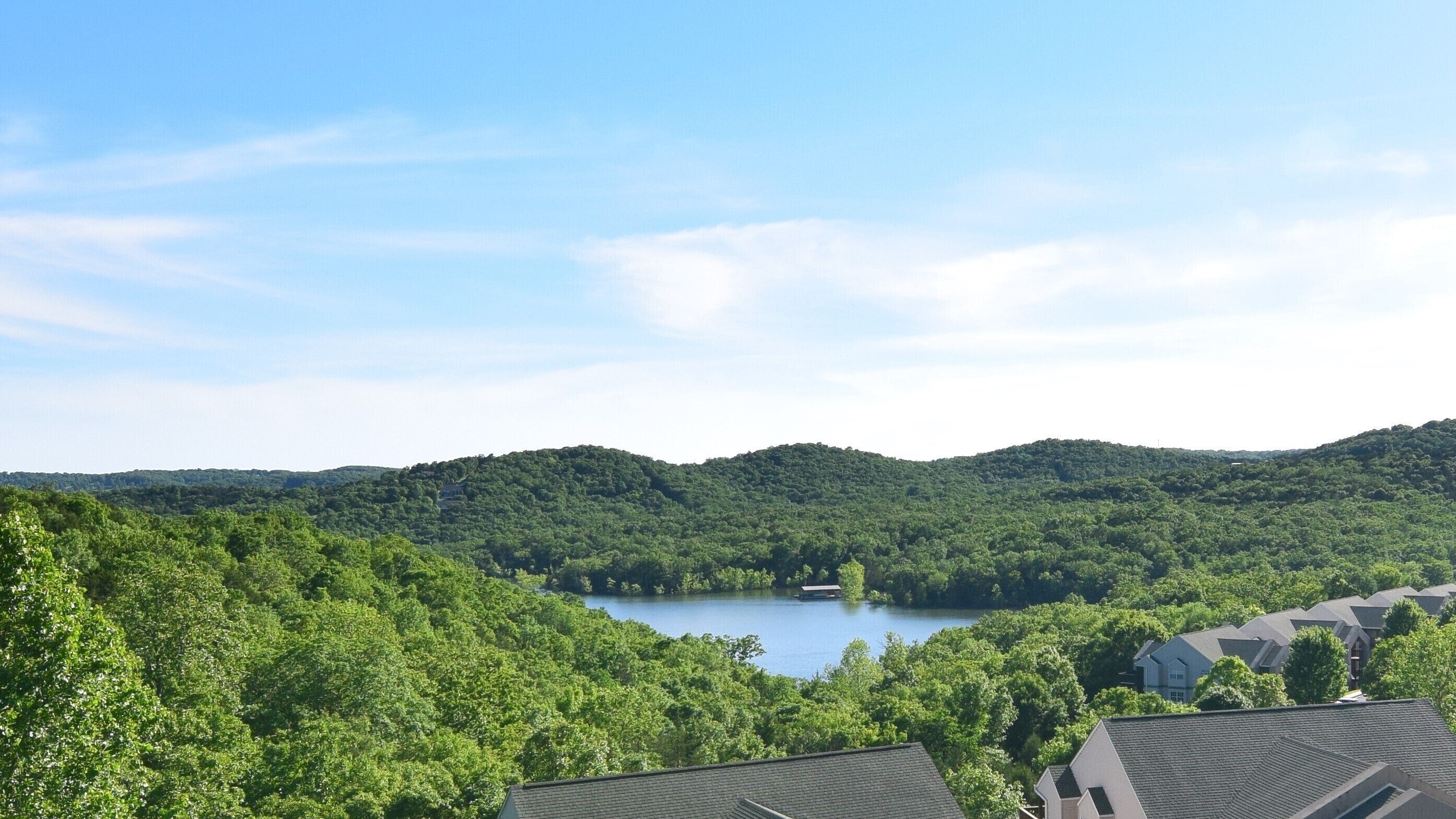 A residential area with houses, a lake, and forested hills.