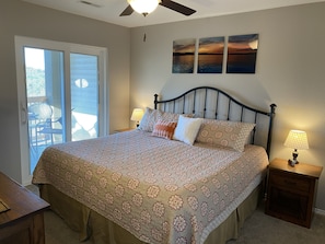 A bedroom with a bed, a ceiling fan, a nightstand with a lamp, and a window with blinds.