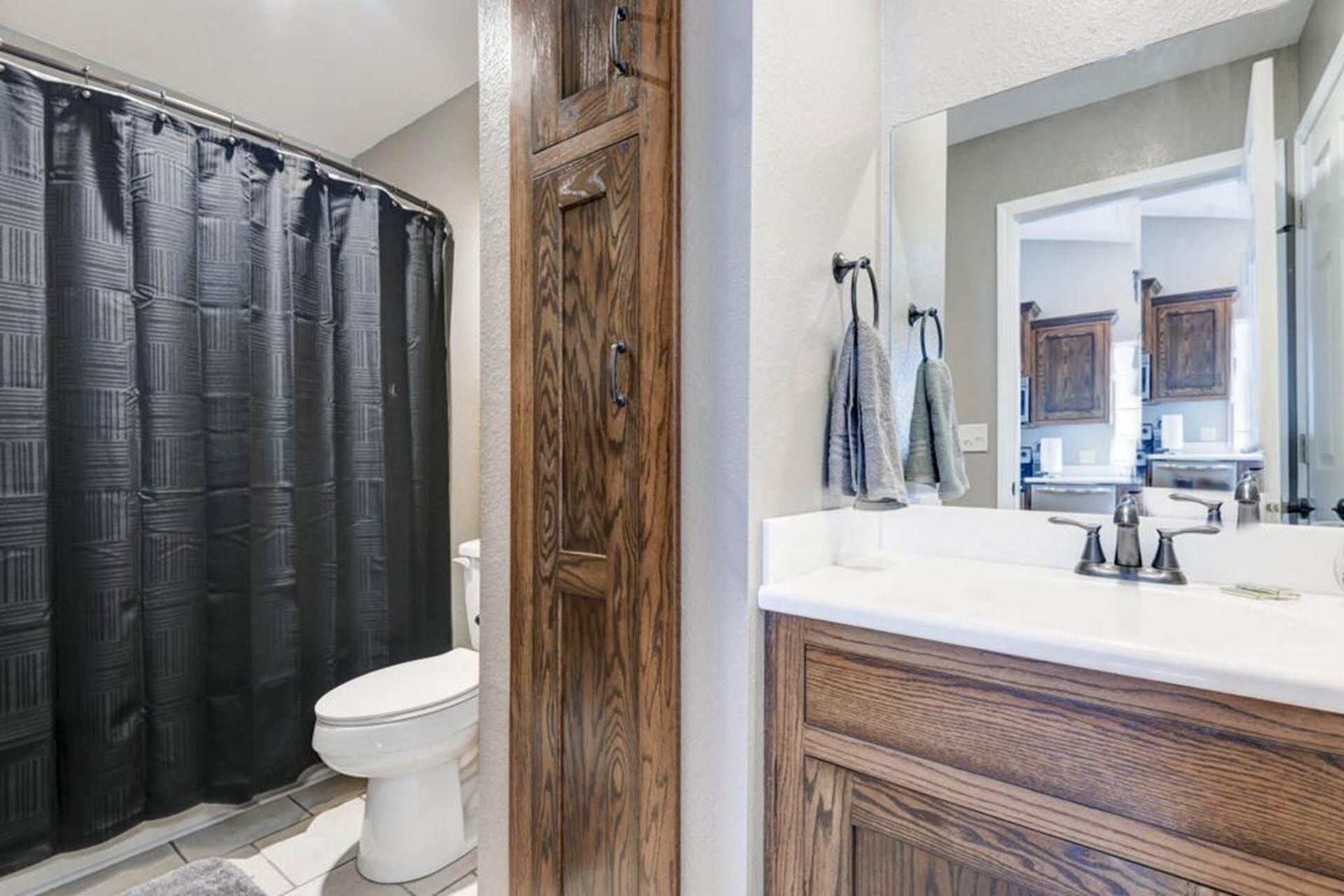 A bathroom with a wooden vanity, a white sink, a mirror, and a shower curtain.