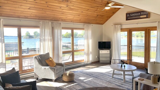 Un vaste salon doté de grandes fenêtres, d’un ventilateur de plafond, d’un téléviseur à écran plat et d’une pancarte indiquant « fleuve Saint-Laurent ».