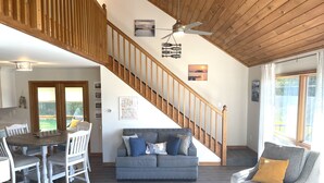 Un vaste espace de vie agrémenté d’un escalier en bois, d’un canapé gris et d’une table à manger avec des chaises.
