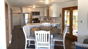 Une cuisine moderne avec des meubles blancs, des appareils en acier inoxydable et une table à manger en bois, assortie de chaises blanches.