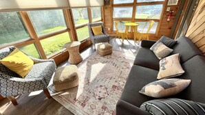 Un intérieur de chalet chaleureux avec un canapé, des fauteuils, une petite table et une vue sur l’extérieur.