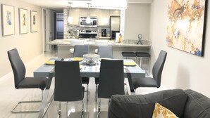 Una cucina moderna con elettrodomestici in acciaio inossidabile, un'area pranzo con un tavolo in vetro e sedie nere, e un grande quadro astratto appeso al muro.