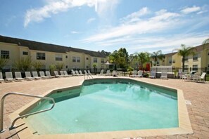 A rectangular pool with a metal ladder, surrounded by lounge chairs and a paved deck.
