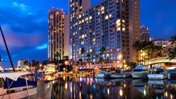 A high-rise hotel with multiple floors and balconies, situated by a marina with boats docked. - Absolutely Oceanfront - Amazing view- Full Kitchen- full disability access. (honolulu)