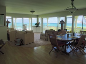 A spacious living area with a view of the ocean, a dining table set for four, and a cozy seating arrangement.