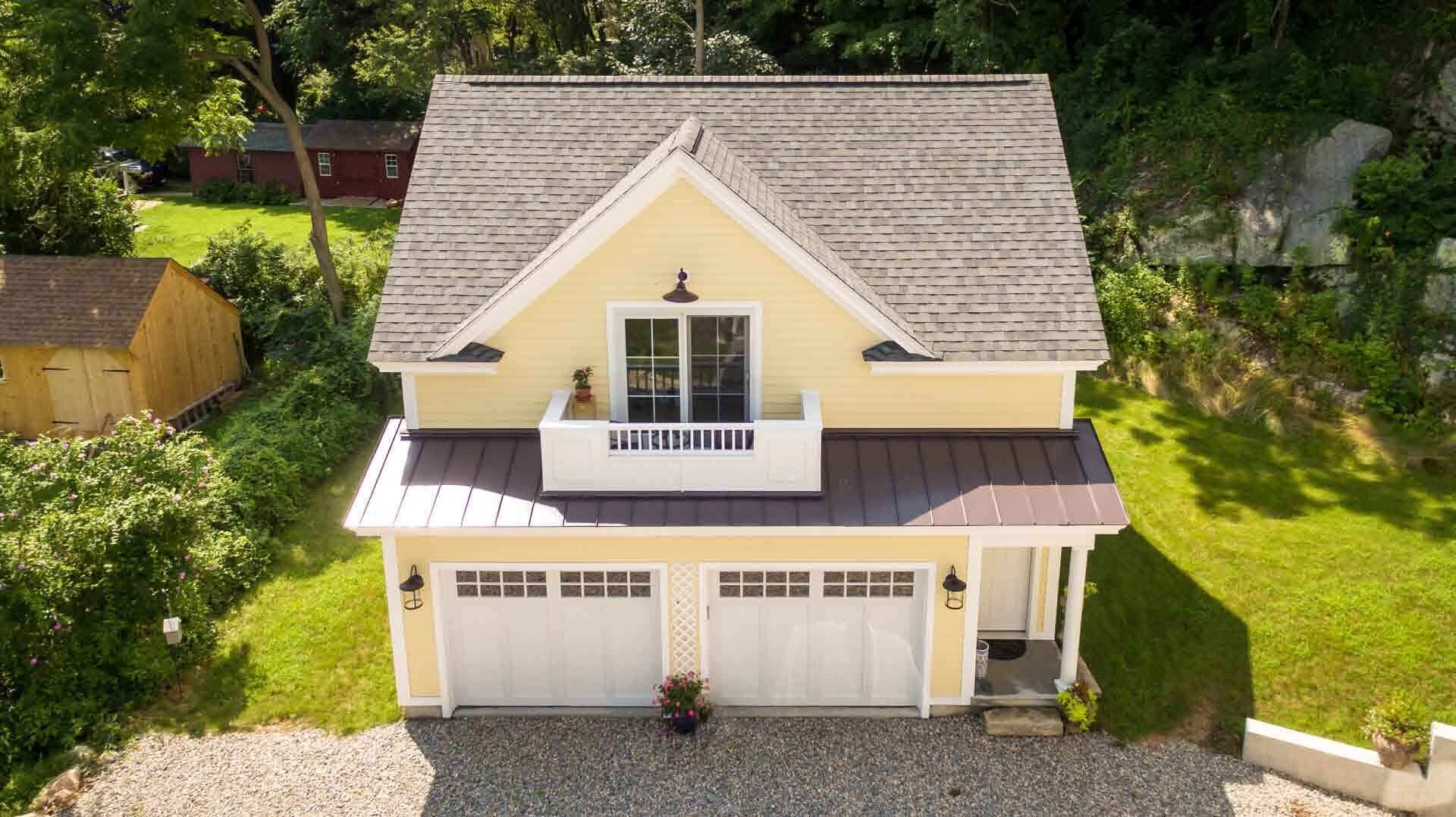 Une maison à deux étages avec un toit à pignon, une véranda à l’avant et un garage.