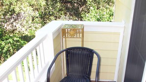A small outdoor balcony with a glass table, two wicker chairs, and a decorative metal chair.