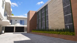 Um edifício moderno com entrada coberta, escadaria e área ajardinada com vegetação.