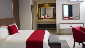 Quarto de hotel com cama, escrivaninha, cadeira, espelho e ar condicionado.
