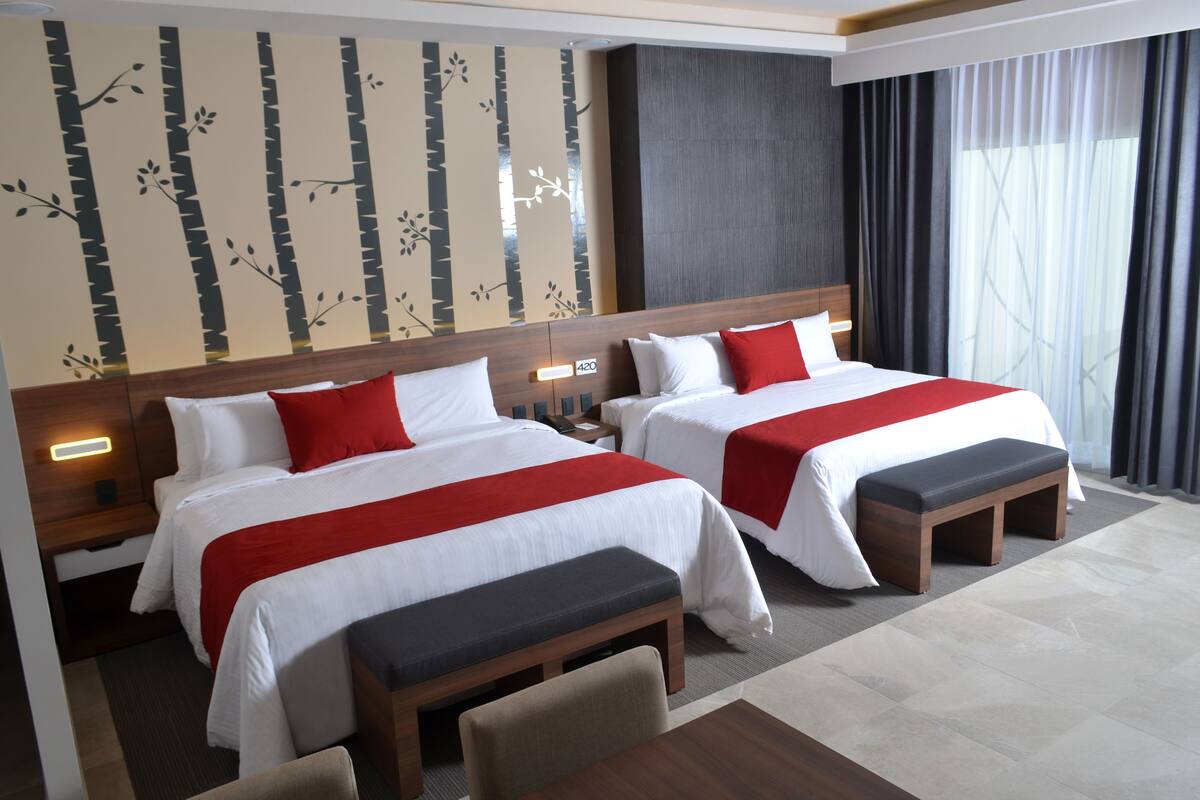 Une chambre d’hôtel avec deux lits, un banc, un bureau et un mur orné d’un motif représentant un arbre.