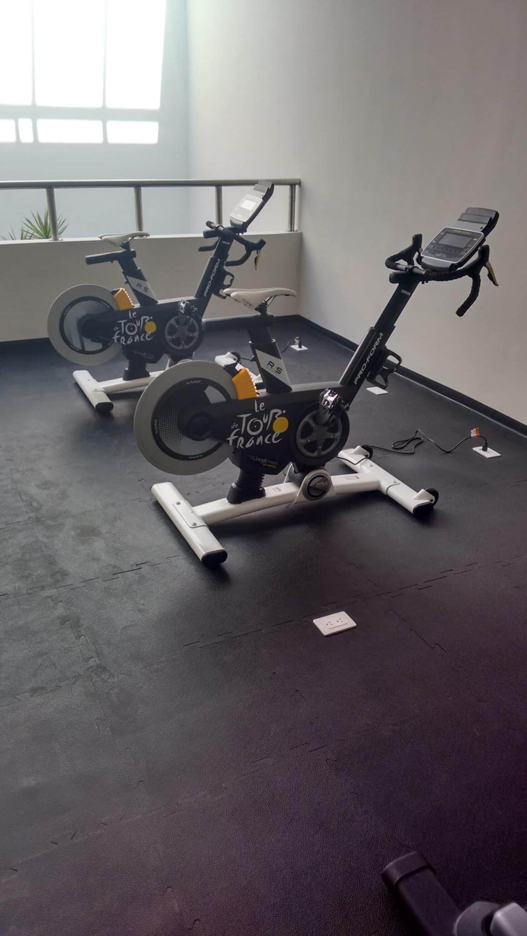 Two stationary bikes in a room with a large window and a power outlet on the floor.