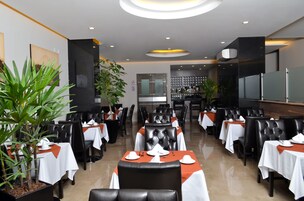 Een restaurant met gedekte tafels, zwarte lederen stoelen en potplanten.