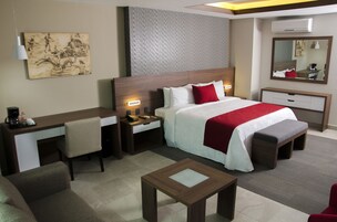 Een hotelkamer met een bed, nachtkastjes, een bureau, een stoel, een klein tafeltje en een grote spiegel.