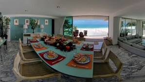 A dining area with a view of the beach, a sofa, and a table with plates and cutlery. - Exclusive & Safe Location: Turquoise Sea w/ White Sand Beach NO SEAWEED (Cancún)