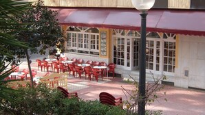 Un espace extérieur aménagé avec des chaises et des tables rouges, un lampadaire et un bâtiment doté de grandes fenêtres et d’un balcon.