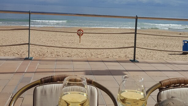 Une vue sur la plage avec une rambarde, une bouée de sauvetage et deux verres posés sur une table.