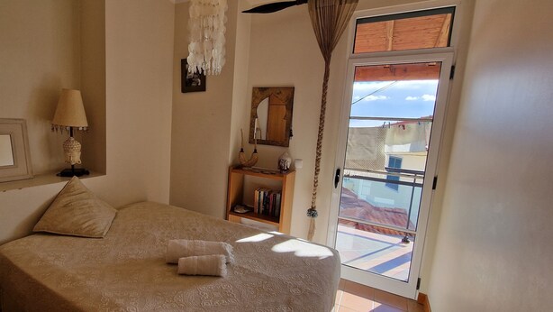 Une chambre à coucher avec un lit, une lampe de chevet, un miroir, une bibliothèque et une vue sur l’extérieur.
