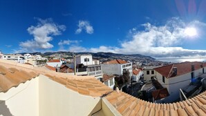 Une ville côtière aux toits de tuiles rouges, sous un ciel dégagé, offrant une vue sur la mer et les montagnes au loin.