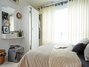 A bedroom with a bed, a bedside table, a wardrobe, a mirror, and a window with curtains. - dcondo Hyde Chiangrai (Chiang Rai)