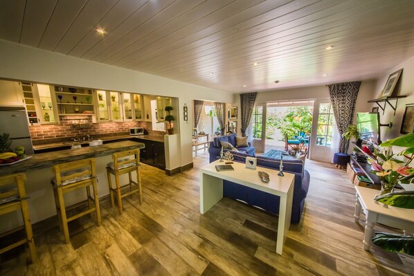 A spacious kitchen with a central island, wooden bar stools, and a dining area with a blue sofa and coffee table.