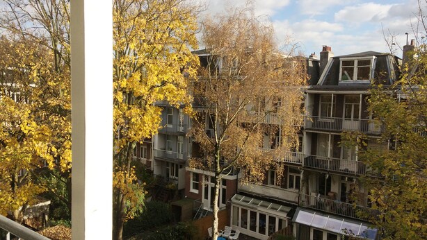 A multi-story residential building with balconies, a covered patio, and a view of surrounding trees. - Just one block from the Jordaan! (Amsterdam)