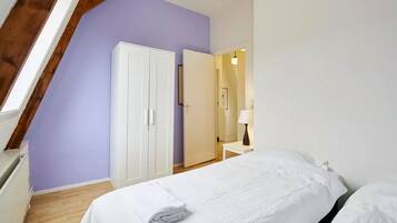 A bedroom with a bed, a wardrobe, and a nightstand with a lamp.