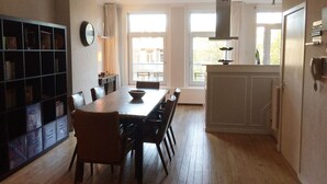 A spacious dining area with a long table and chairs, a bookshelf, and a view of the outside through large windows. - Just one block from the Jordaan! (Amsterdam)