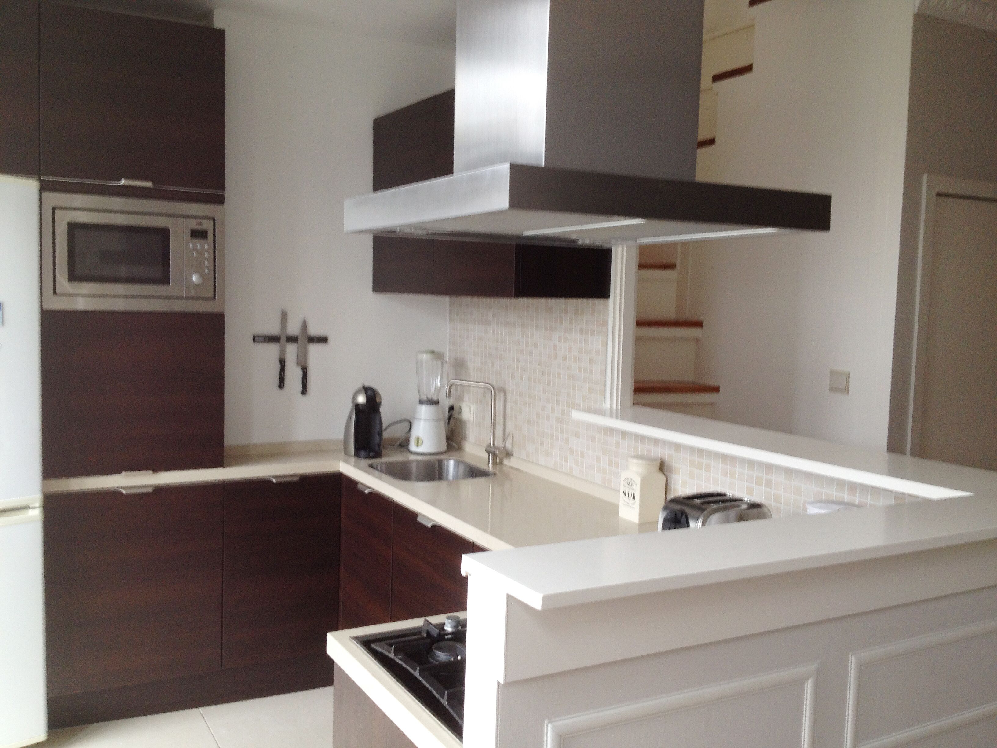 Una cocina moderna con armarios de madera oscura, microondas de acero inoxidable, cocina empotrada y encimera blanca.