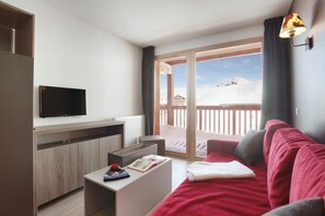 A modern living room with a flat-screen TV, a wooden cabinet, a red sofa, a white coffee table, and a balcony with a view of a snowy landscape.