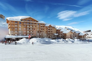 Ein verschneites Skigebiet mit mehrstöckigen Holzhäusern, Seilbahnen und blauem Himmel.