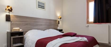 Une chambre à coucher avec un lit, des tables de chevet, une lampe, un tableau au mur et une fenêtre avec des rideaux.