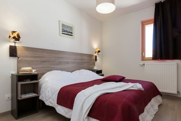 A bedroom with a bed, nightstands, a lamp, a picture on the wall, and a window with curtains.