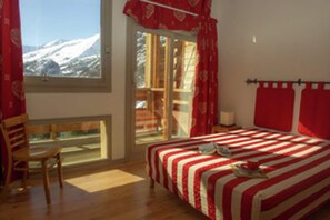 Une chambre à coucher avec un lit, une chaise, une fenêtre donnant sur les montagnes et un balcon.
