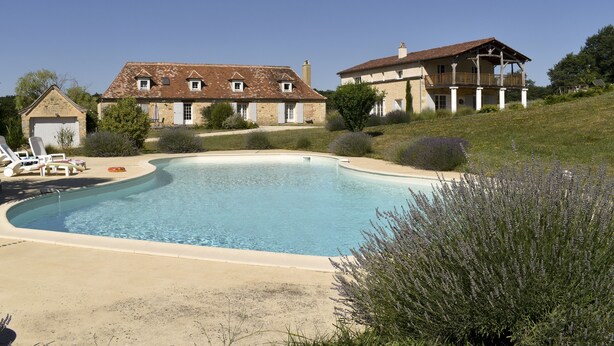 A large swimming pool surrounded by a house with a balcony and a garage. - Le Domaine des Ravels, 4-star charm and comfort, calm and relaxation in the countryside (Cause-De-Clérans)