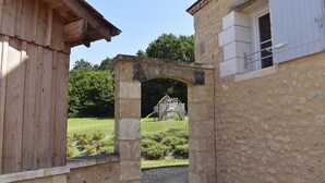 An arched stone gateway leading to a wooden building with a window. - Le Domaine des Ravels, 4-star charm and comfort, calm and relaxation in the countryside (Cause-De-Clérans)