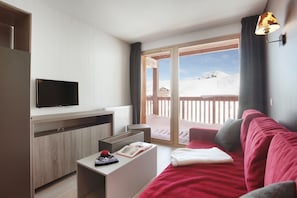 A modern living room with a flat-screen TV, a wooden cabinet, a red sofa, a white coffee table, and a balcony with a view of a snowy landscape.