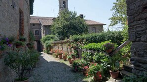 Un callejón adoquinado con edificios de piedra, una torre de campanas y plantas en macetas.