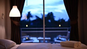 A hotel room with a bed, a hanging light fixture, and a view of a balcony with tables and chairs. - Sabye D Resort at Surat (Surat Thani)
