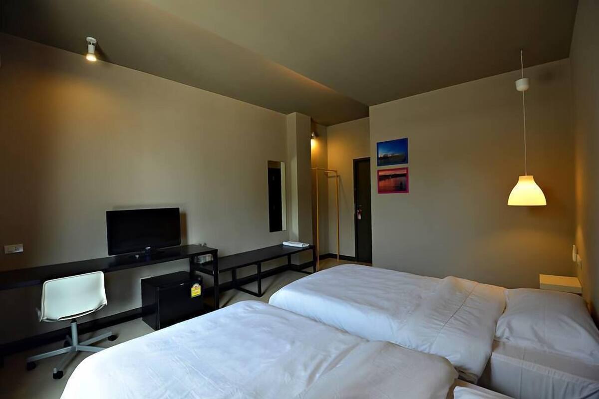 Une chambre d’hôtel avec deux lits, un bureau avec une chaise, une télévision et un luminaire fixé au mur.