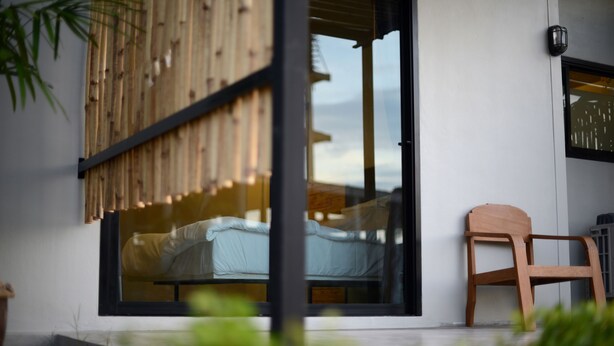 A modern room with a large sliding glass door, a wooden chair, and a bed with a white cover. - Sabye D Resort at Surat (Surat Thani)