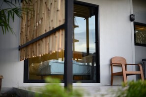 A modern room with a large sliding glass door, a wooden chair, and a bed with a white cover. - Sabye D Resort at Surat (Surat Thani)