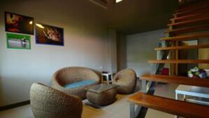A modern living room with a sofa, armchair, and ottoman. There is a staircase with wooden steps and a small table with a vase of flowers. - Sabye D Resort at Surat (Surat Thani)