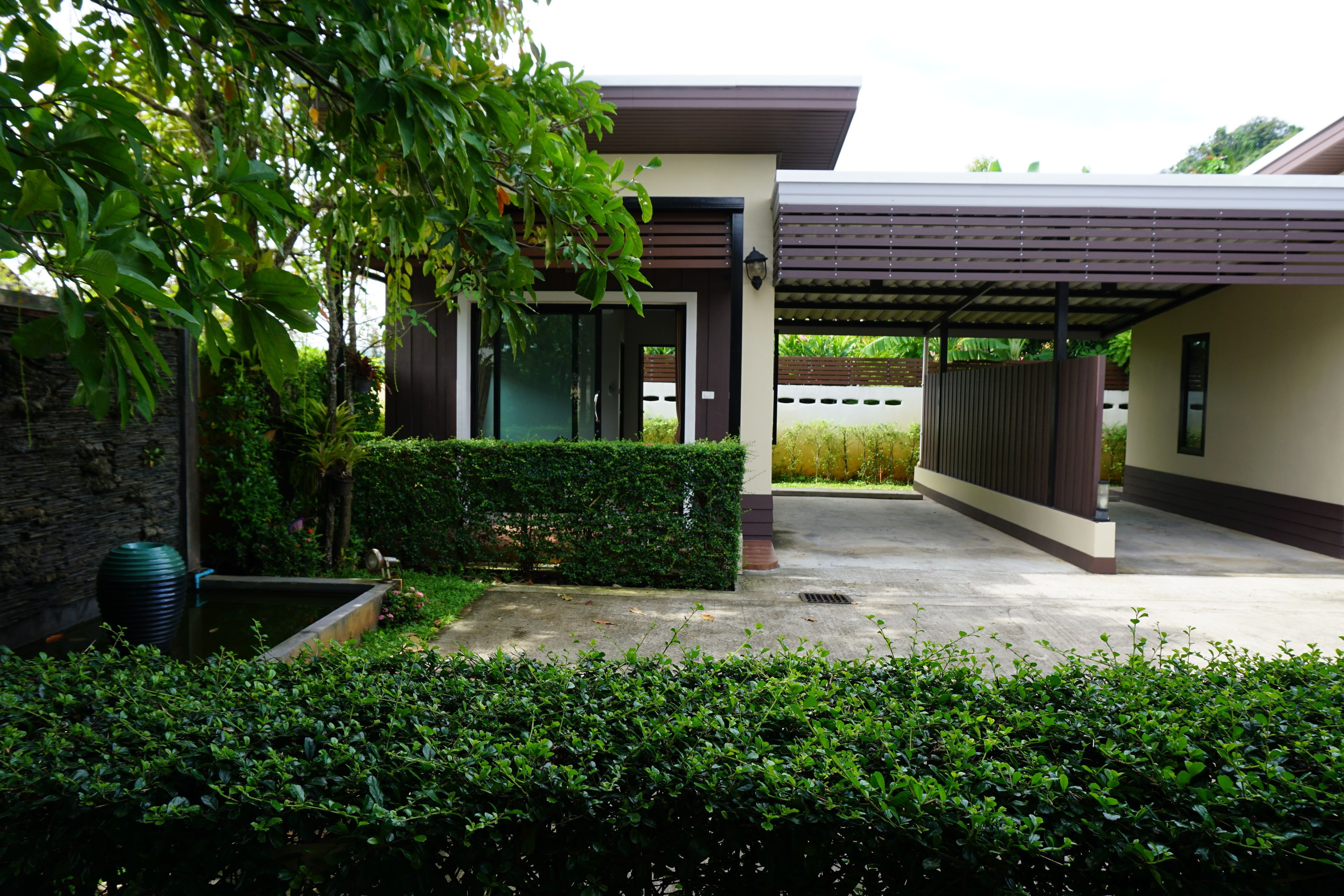 A modern house with a covered patio, a stone wall, and a well-maintained garden.