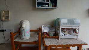 Una silla de madera con una mesa, una tetera, un mueble bajo y un teléfono en la pared.